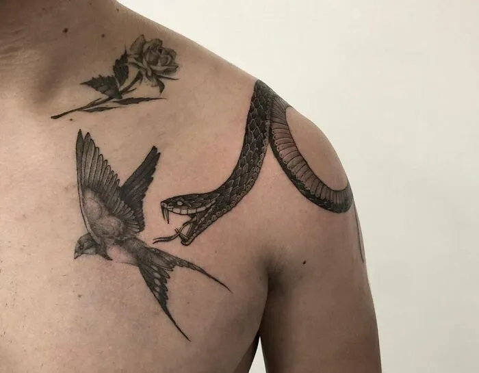 Snake tattoo on shoulder with rose and bird design in black ink.