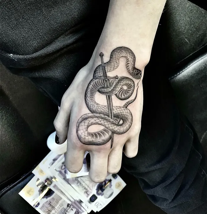 Snake tattoo on a hand, featuring a detailed design of a snake wrapped around a dagger.