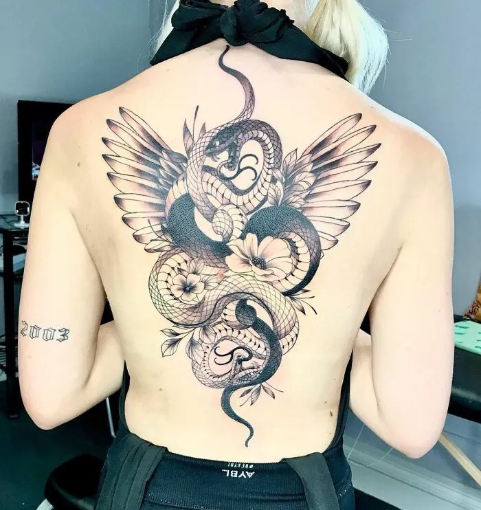 Intricate snake tattoo on a woman's back, featuring wings and flowers.