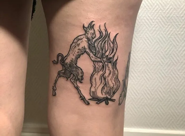 Gothic tattoo depicting a whimsical creature interacting with a stylized fire on skin.
