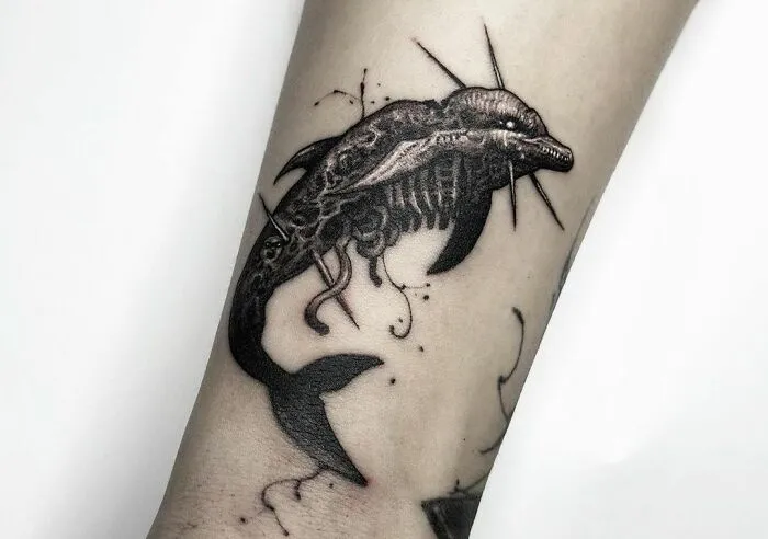 Forearm with an intricate gothic tattoo of a dolphin skeleton design.
