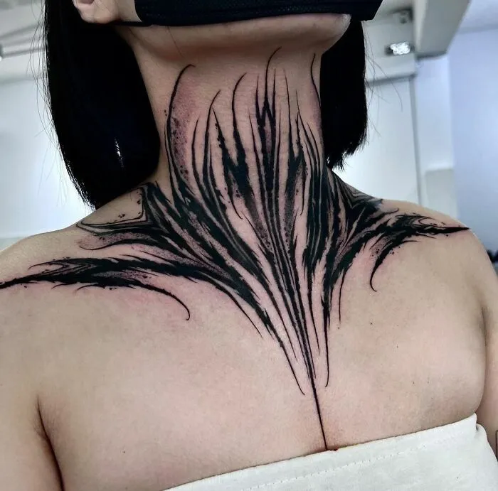 Gothic tattoo design on neck and chest, featuring bold black lines and intricate patterns.