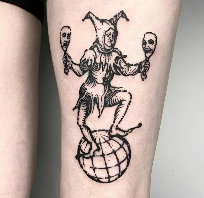 Gothic tattoo of a jester balancing on a globe, holding two masks.