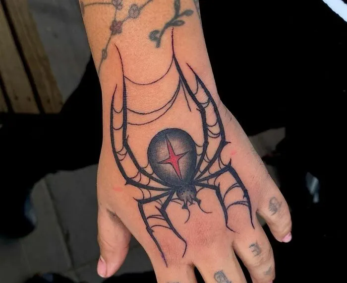 Hand with a gothic tattoo of a spider with web details, showcasing intricate design elements.