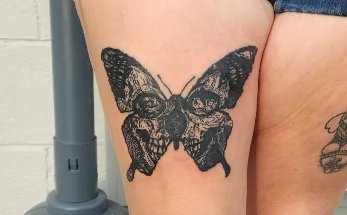Gothic tattoo of a black butterfly with skull motifs on the wings, inked on an arm.