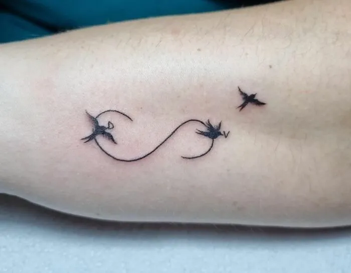 Infinity tattoo with birds symbolizing eternal creativity on arm.