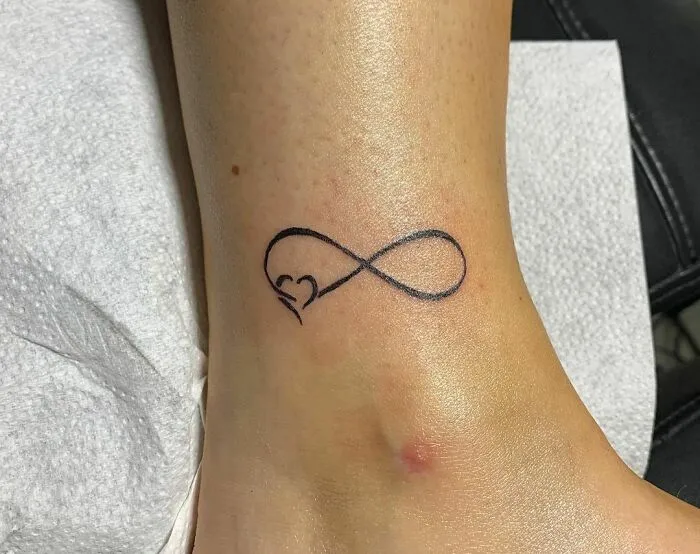 Infinity tattoo on ankle with heart detail, showcasing creativity and eternal symbolism.