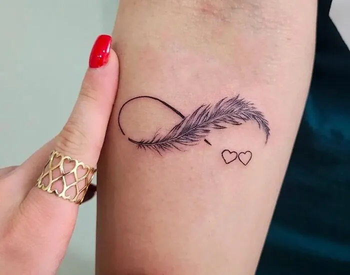 Infinity tattoo with a feather and hearts, showcasing eternal creativity on a person's arm.