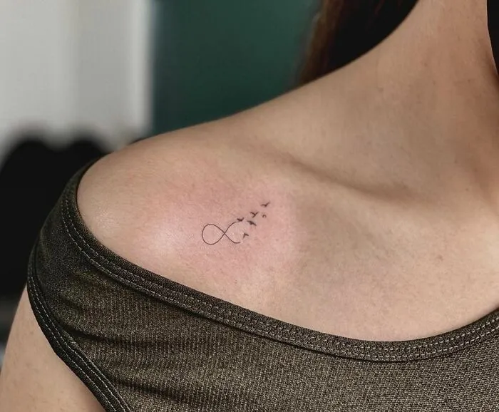 Infinity tattoo with birds on shoulder, symbolizing eternal creativity.