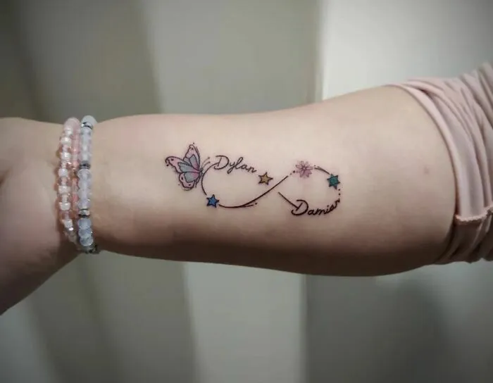 Infinity tattoo featuring butterfly and stars on forearm, symbolizing creativity.