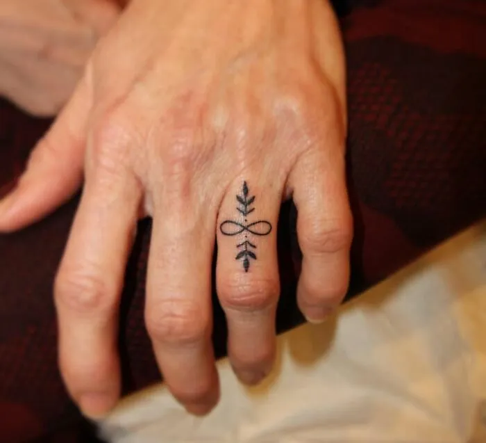 Infinity tattoo with leaf design on a finger, symbolizing eternal creativity.