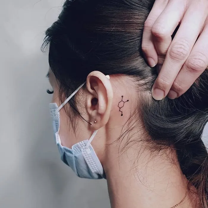 Small tattoo behind the ear representing mental health in a minimalist design, woman wearing a mask.