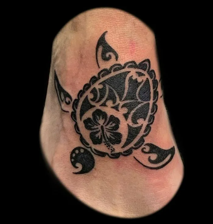 Black tribal tattoo of a turtle on foot, showcasing intricate patterns and design elements.