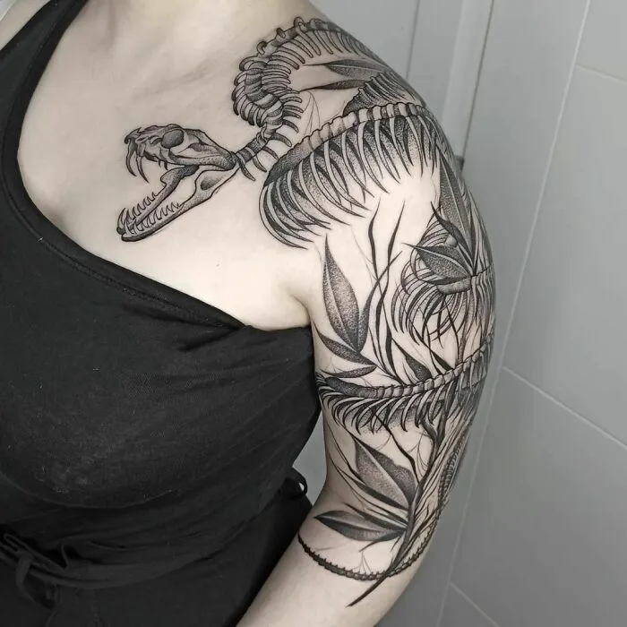 Snake tattoo design on upper arm featuring detailed skeletal and leaf patterns.
