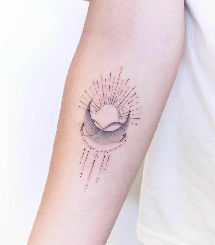 Infinity tattoo with crescent moon and sunburst lines on forearm.