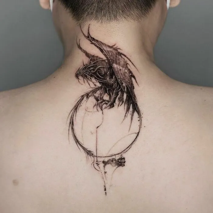 Gothic tattoo of a detailed dragon on a person's upper back, showcasing intricate artwork and dark themes.