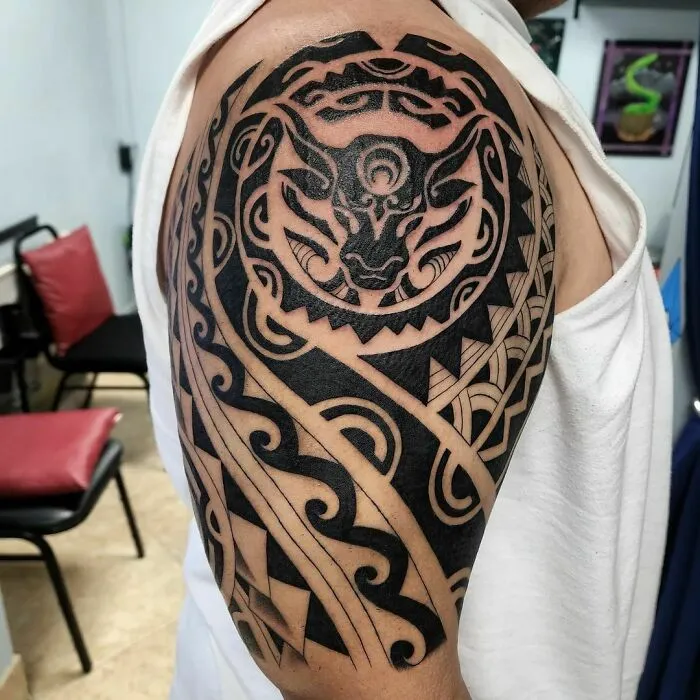 A detailed tribal tattoo featuring intricate animal and geometric patterns on an upper arm.
