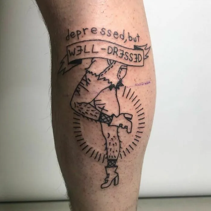 Mental health tattoo on leg saying "depressed, but well-dressed" with a line art design.
