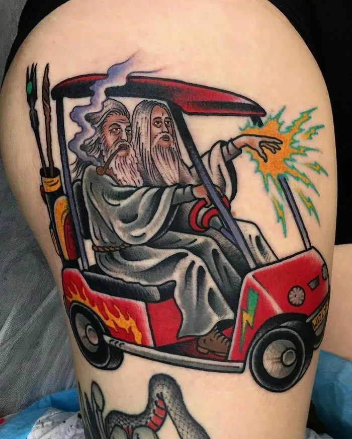 Tattoo of two wizard-like characters on a golf cart, one casting magic, embodying Lord of the Rings themes.