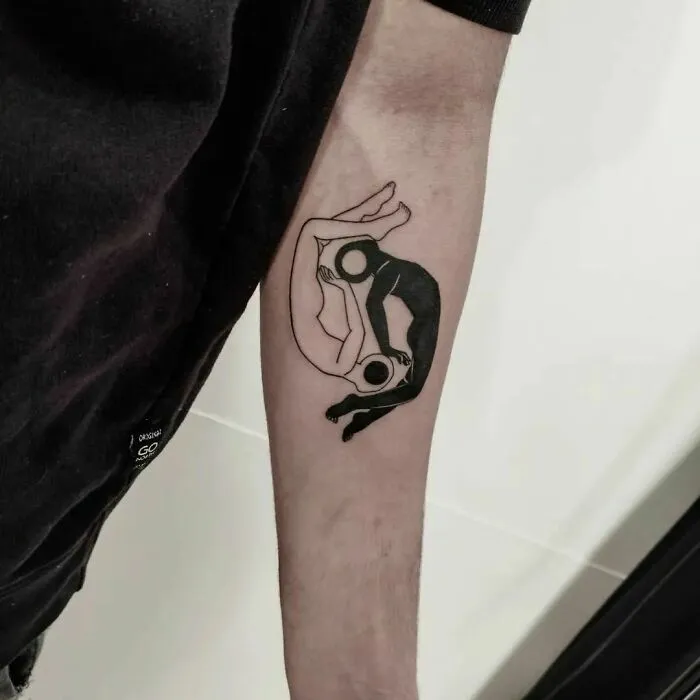 Minimalist Yin Yang tattoo on a forearm, featuring black and white figures symbolizing duality.