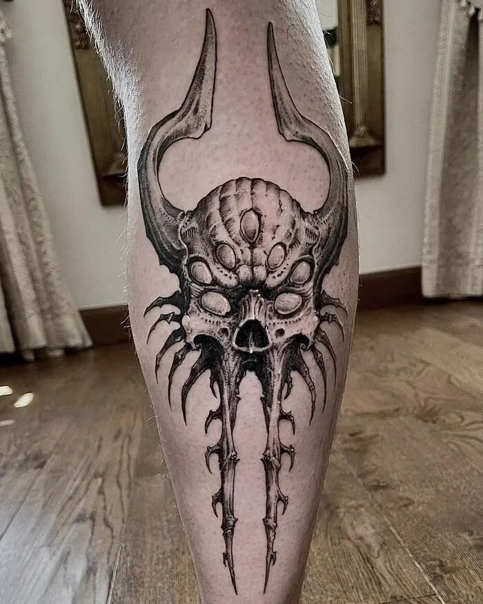 Intricate gothic tattoo design featuring a horned skull with symmetrical patterns on a person's calf.