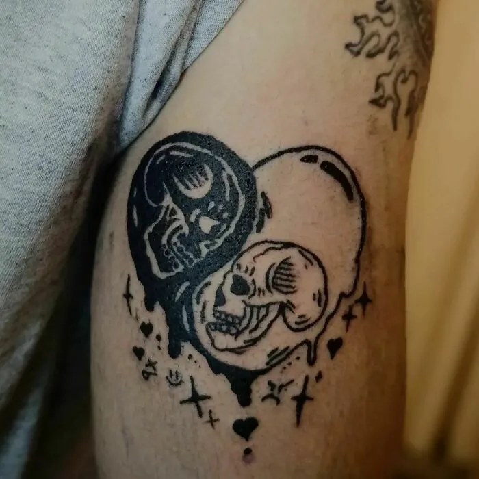 Yin Yang tattoo with skulls symbolizing life's duality on an arm.