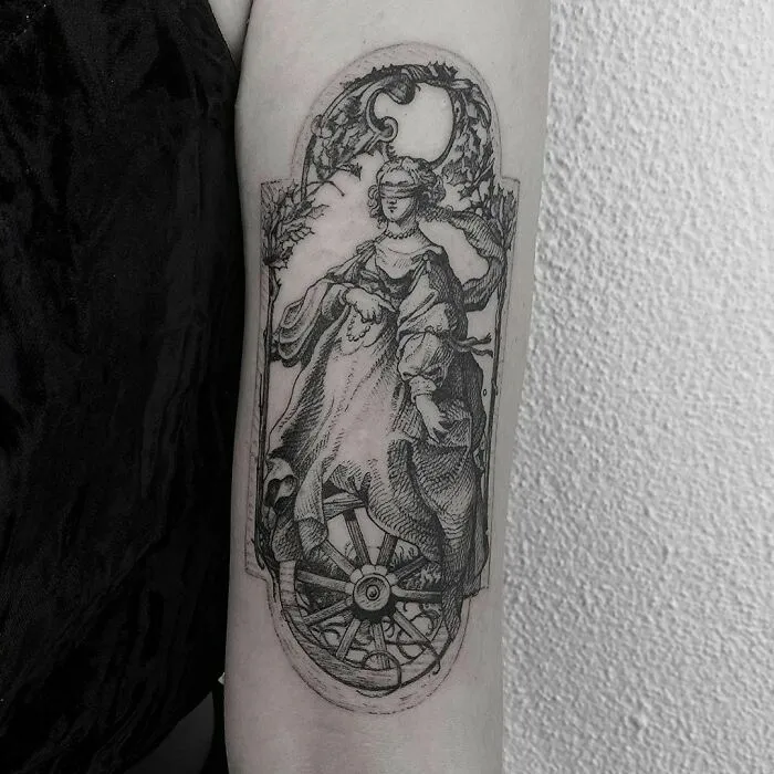 Black and white gothic tattoo depicting a classical figure with a skull and wheel detail on forearm.