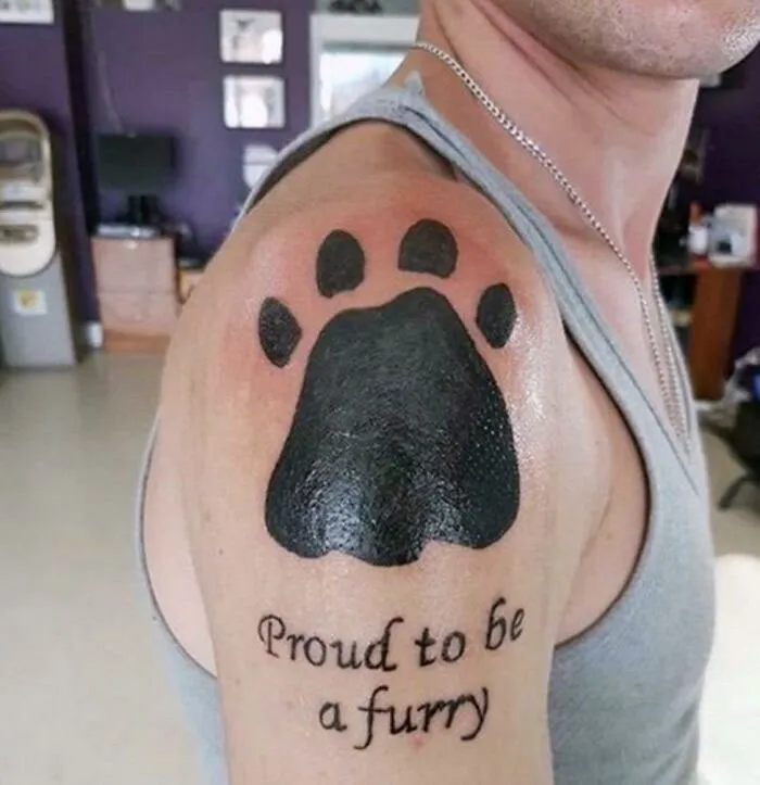 Tattoo of a large paw print and "Proud to be a furry" text on shoulder; a permanent ink choice.