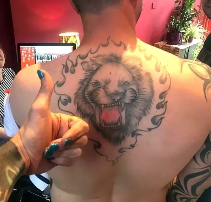 Back tattoo of a lion with flames; a permanent ink mistake earning a thumbs-up in a tattoo studio setting.