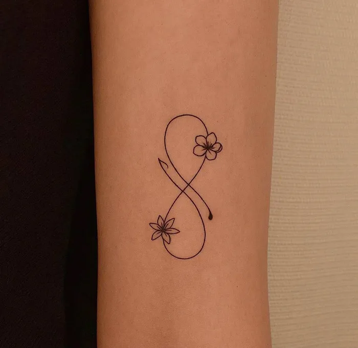 Infinity tattoo on forearm with floral accents, embodying eternal creativity.