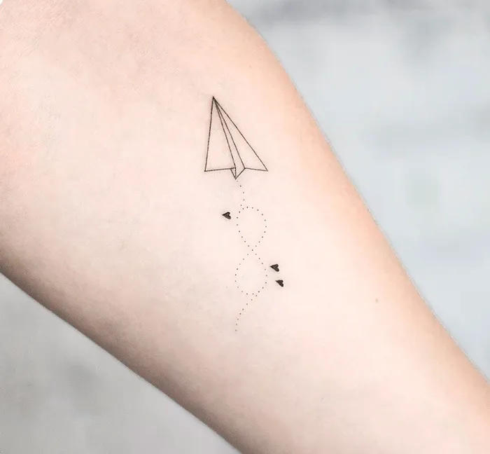 Minimal paper plane infinity tattoo symbolizing eternal creativity.