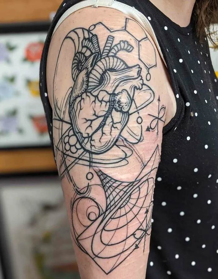 Science tattoo featuring a heart, atomic symbols, and geometric patterns on a person's upper arm.