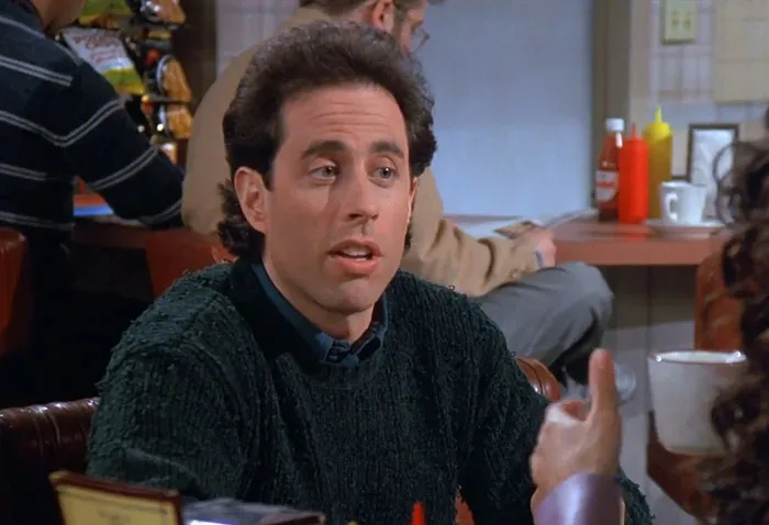 Jerry wearing a black sweater in a sitcom scene illustrating funniest Seinfeld quotes that sum up everyday life.