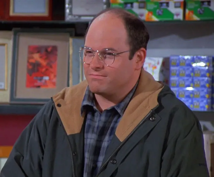George wearing a black jacket and blue-gray shirt in a classic scene featuring funniest Seinfeld quotes about everyday life.