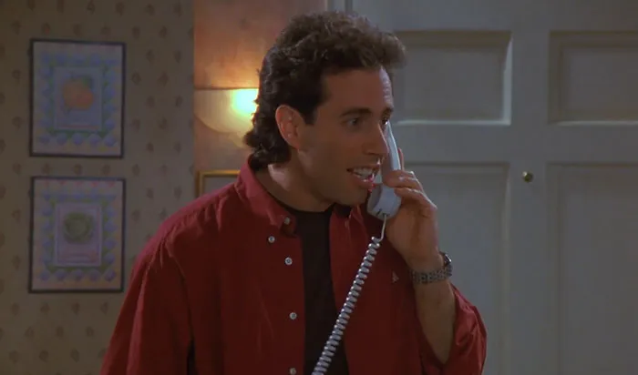 Jerry from Seinfeld wearing a red shirt, speaking on a phone, illustrating funniest Seinfeld quotes about everyday life.