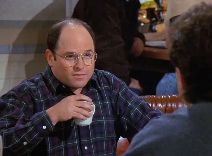 George from Seinfeld wearing a colorful shirt while enjoying a coffee, illustrating funniest Seinfeld quotes about everyday life.
