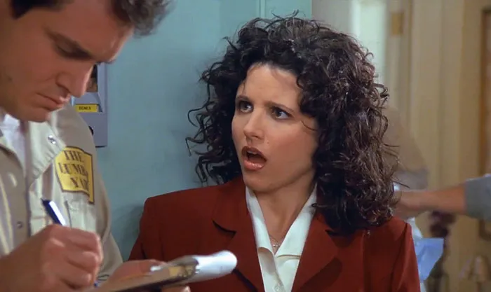 Elaine wearing white shirt and red suit reacting with surprise, illustrating funniest Seinfeld quotes about everyday life.