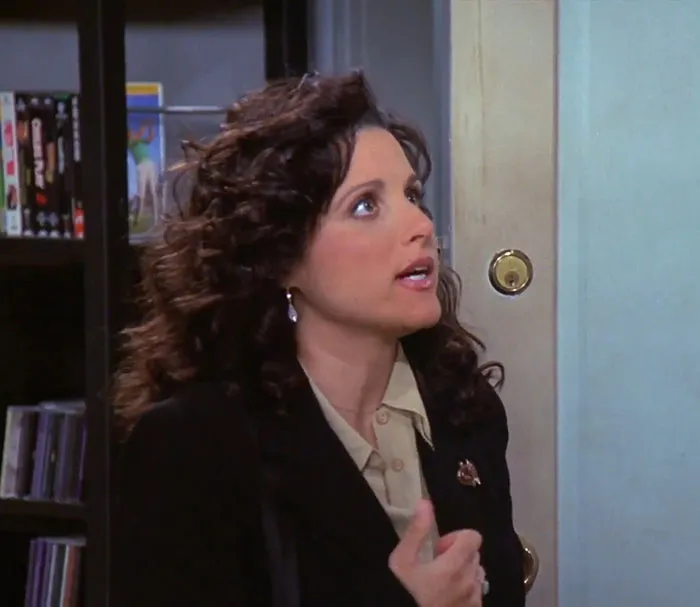 Elaine from Seinfeld wearing a black jacket and brown shirt, expressing one of the funniest Seinfeld quotes about everyday life