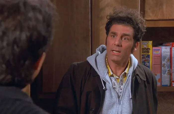 Cosmo Kramer wearing brown jacket and gray hoodie, delivering some of the funniest Seinfeld quotes about everyday life.