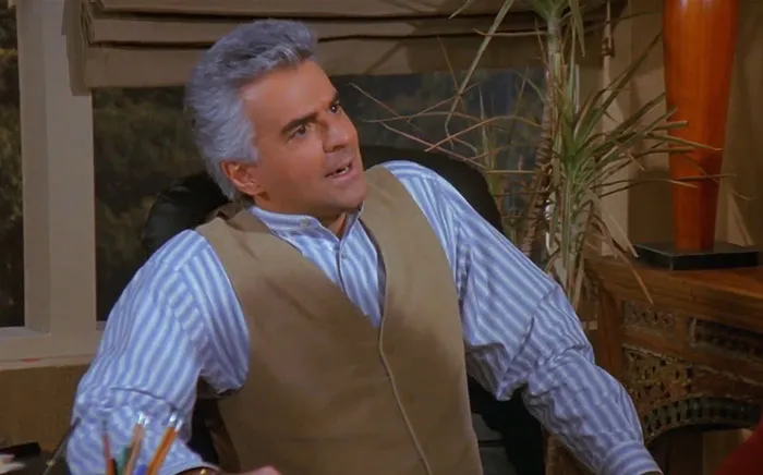 J. Peterman wearing brown vest and blue striped shirt, representing funniest Seinfeld quotes about everyday life.