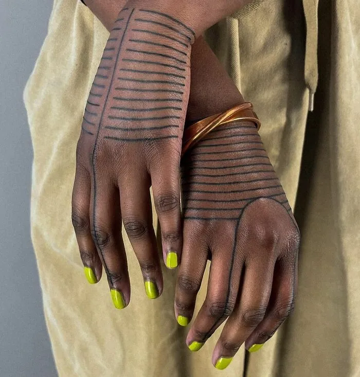 Close-up of hands with tribal tattoo patterns and green nails, featuring brown bangles.