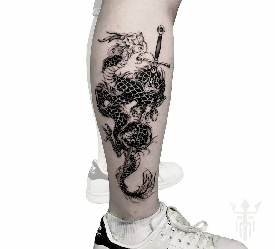 Black dragon tattoo design on a leg with sword detail, showcasing intricate ink work.