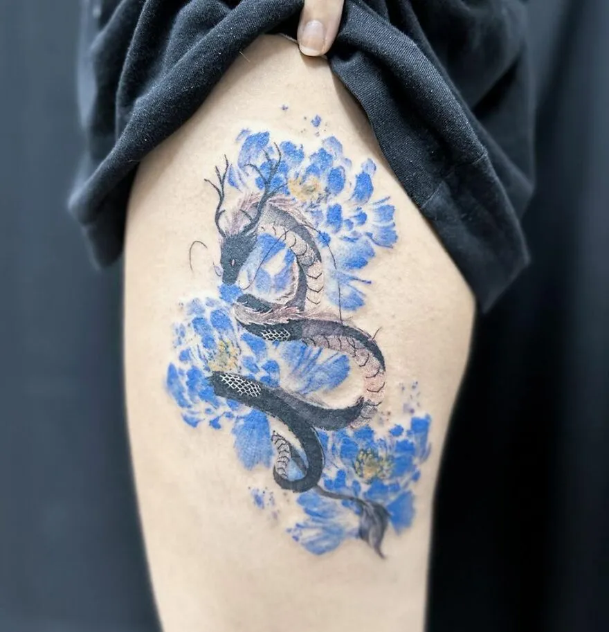 Dragon tattoo with blue floral background on upper thigh.