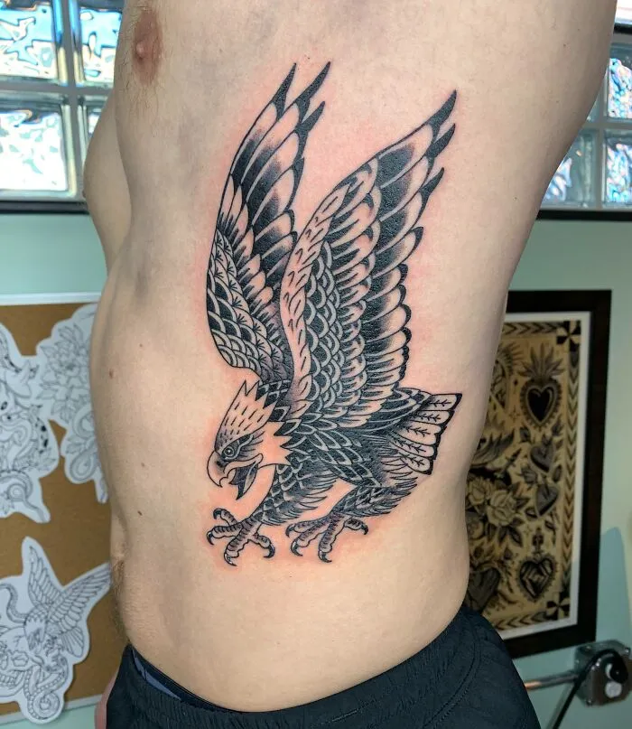 American traditional tattoo of a detailed black and grey eagle on a person's side.