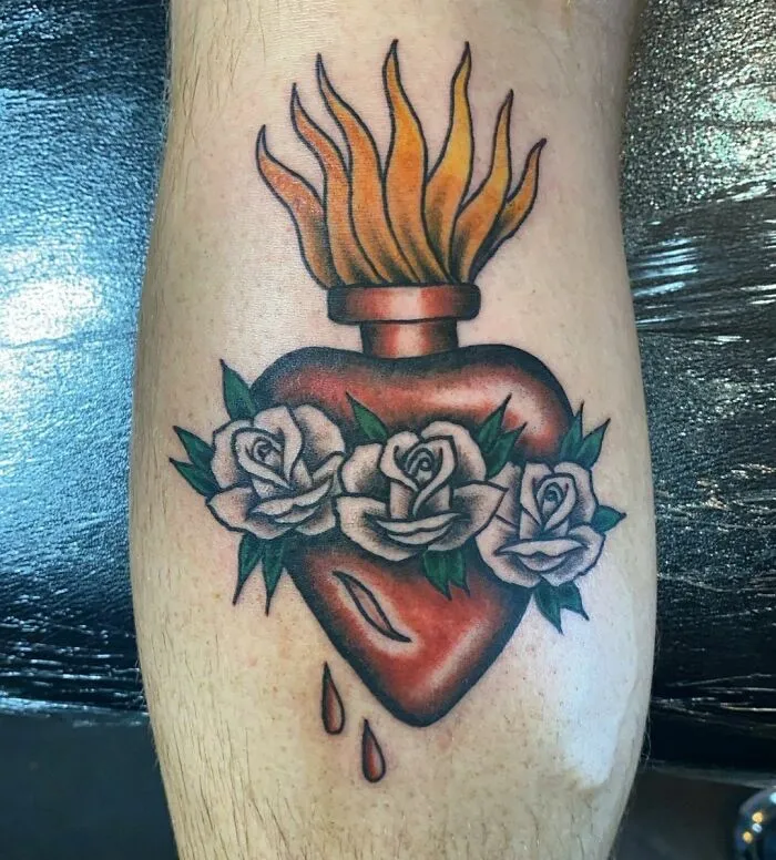 American traditional tattoo of a flaming heart with white roses and dripping blood on skin.