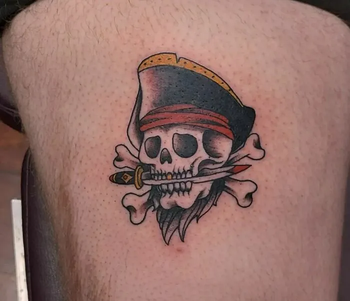 American traditional tattoo featuring a pirate skull with a dagger in its mouth, showcasing bold colors and classic design.