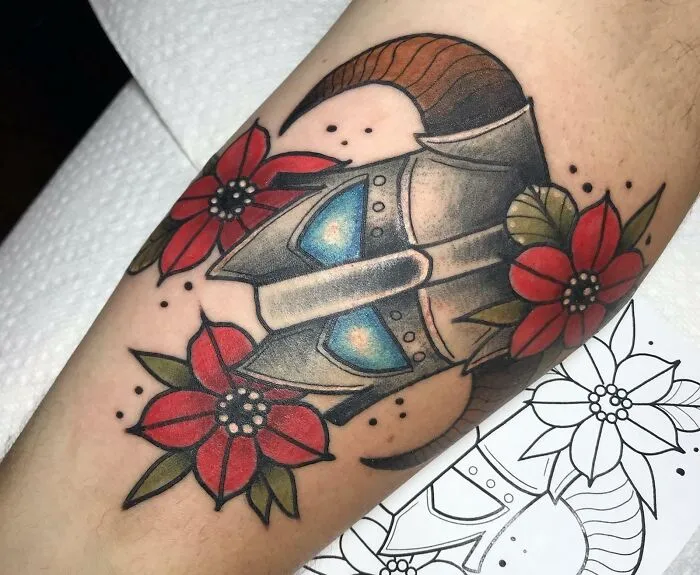 Arm with American traditional tattoo featuring a horned helmet and red flowers.