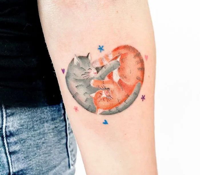 Yin Yang tattoo with two intertwined cats on an arm, symbolizing duality and balance.