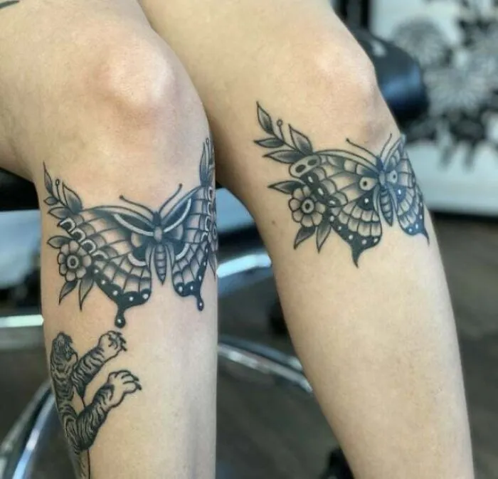 Butterfly tattoos on knees with floral accents, showcasing artistic detail and design.