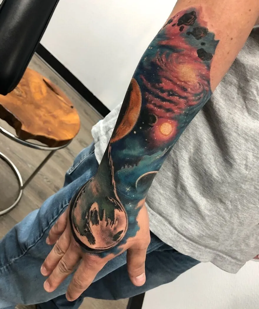 Colorful space tattoo featuring planets and galaxies on a forearm, showcasing outer space artistry.